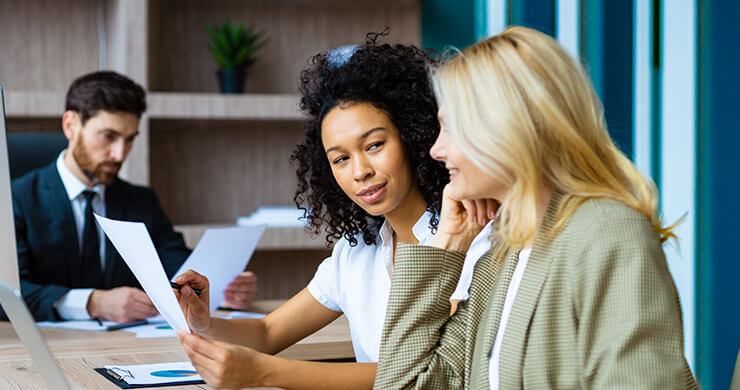 Two women discussing documents in a modern office setting.