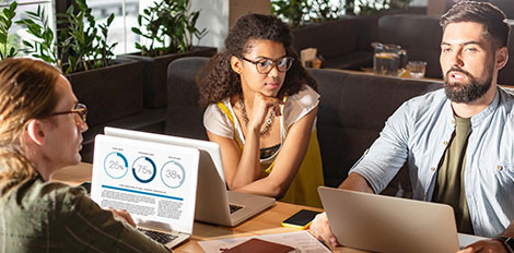 Three colleagues discussing data in a modern office with laptops.