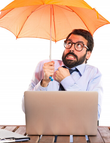 Nervous man holding an orange umbrella over a laptop at a desk.