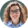 Smiling woman with curly hair and glasses in a blue shirt.