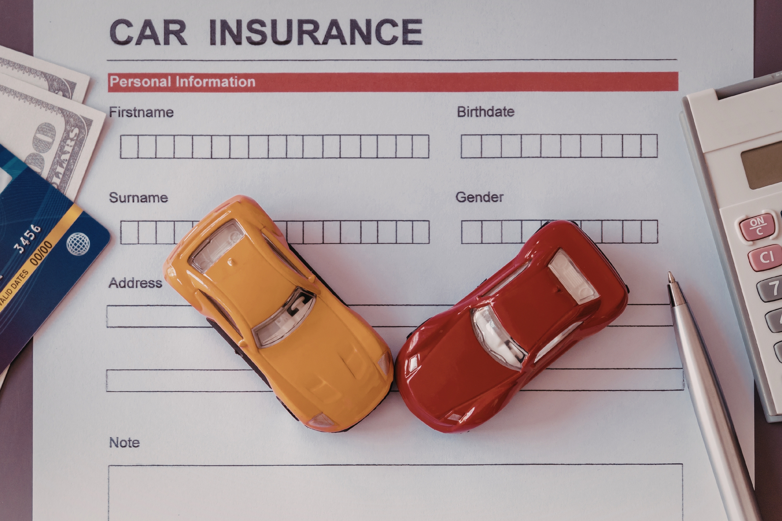 Car insurance form with toy cars, money, credit card, calculator, and pen.