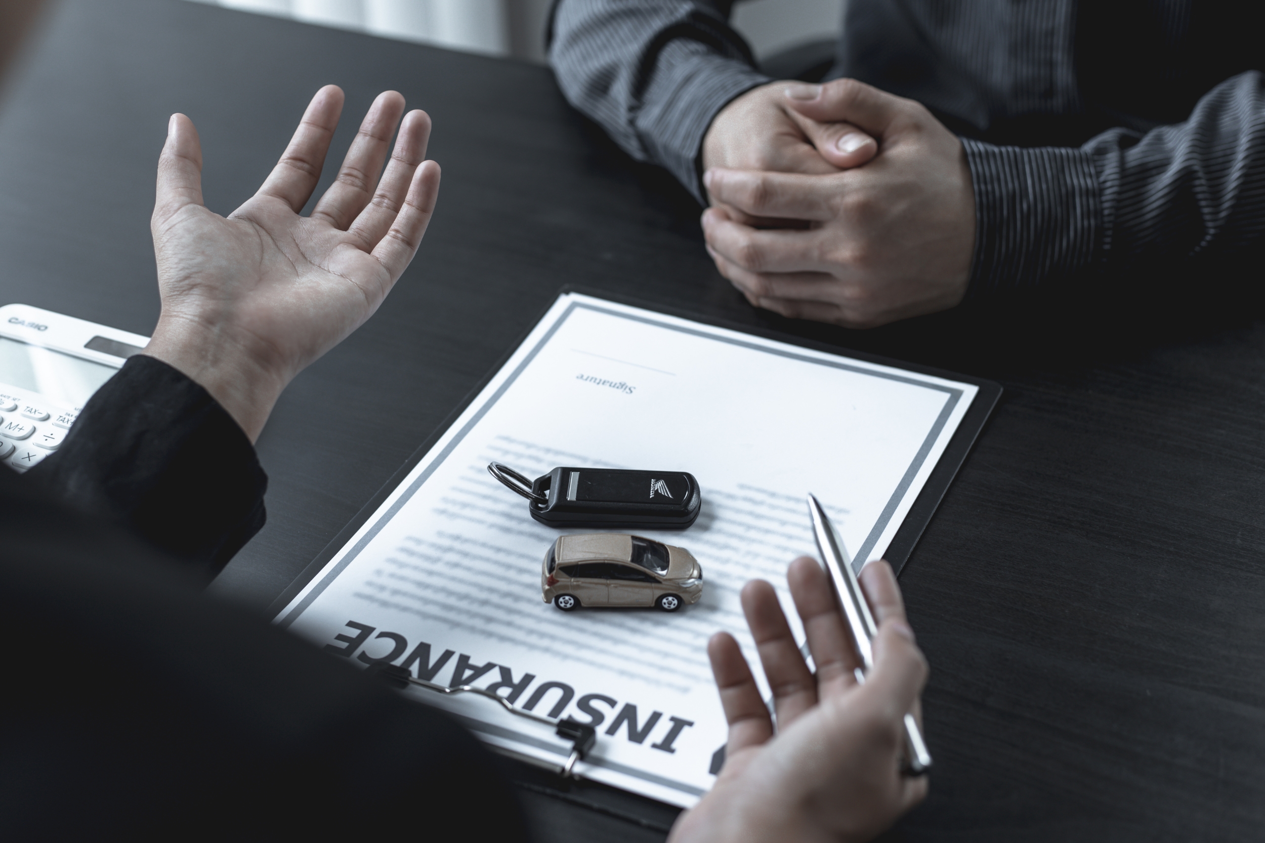 Two people discussing car insurance with keys and model car on a contract.