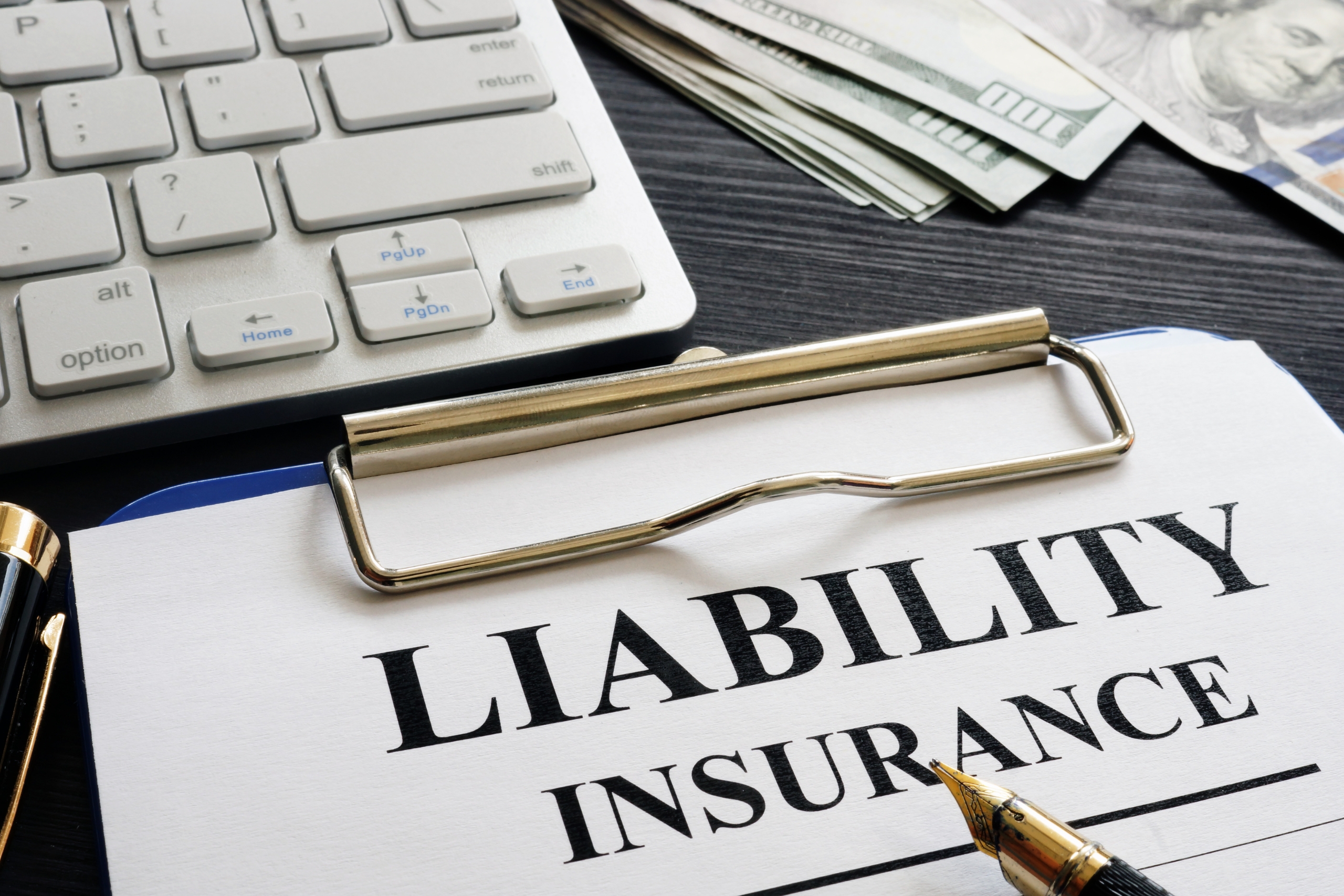 Liability insurance document on a clipboard with a pen and keyboard.