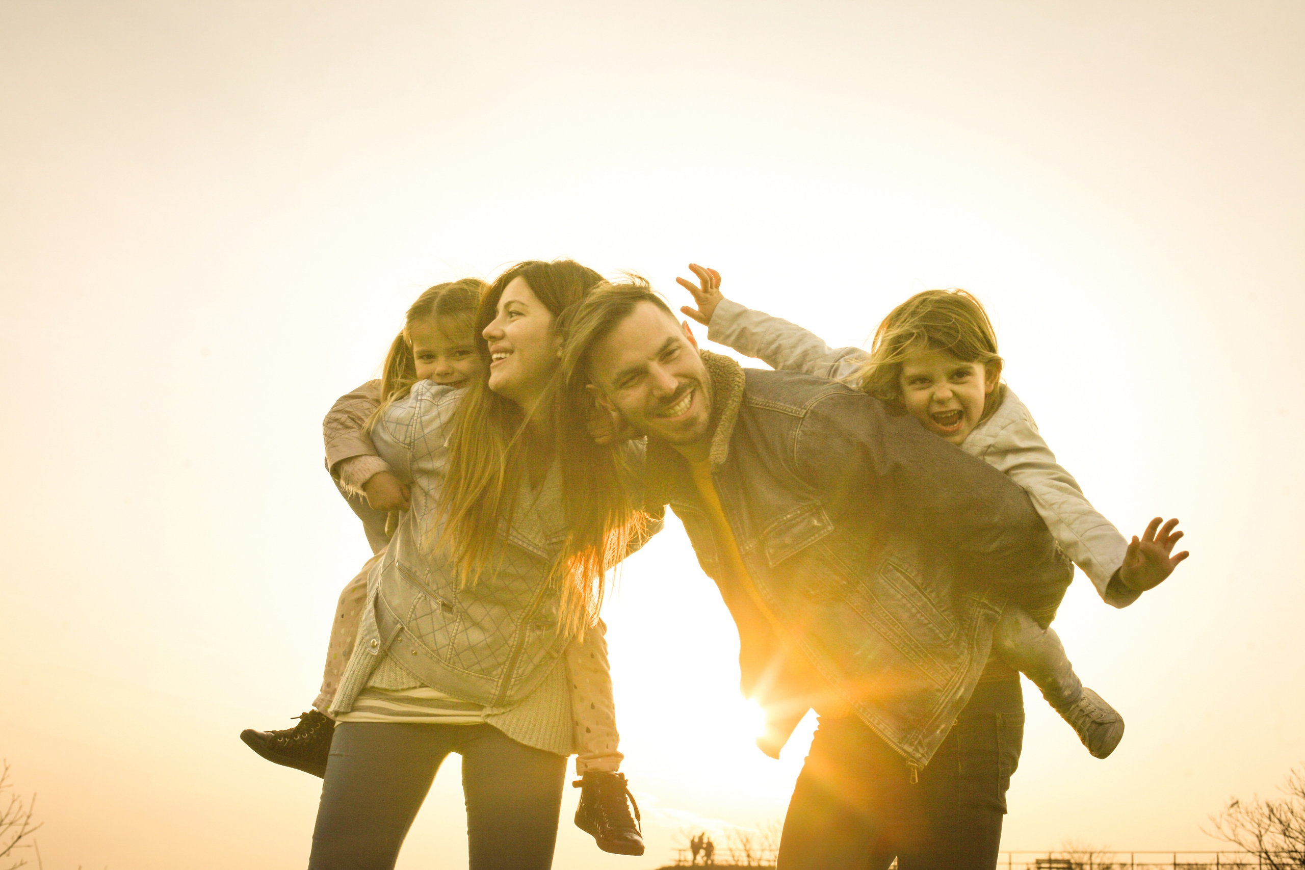 Happy parents giving piggyback rides to their joyful children at sunset.