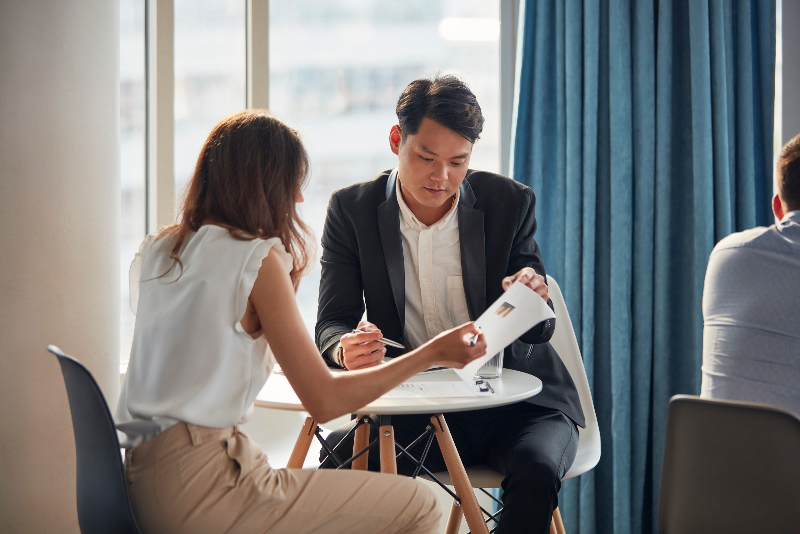 Two professionals discussing documents at a small round table near a window.