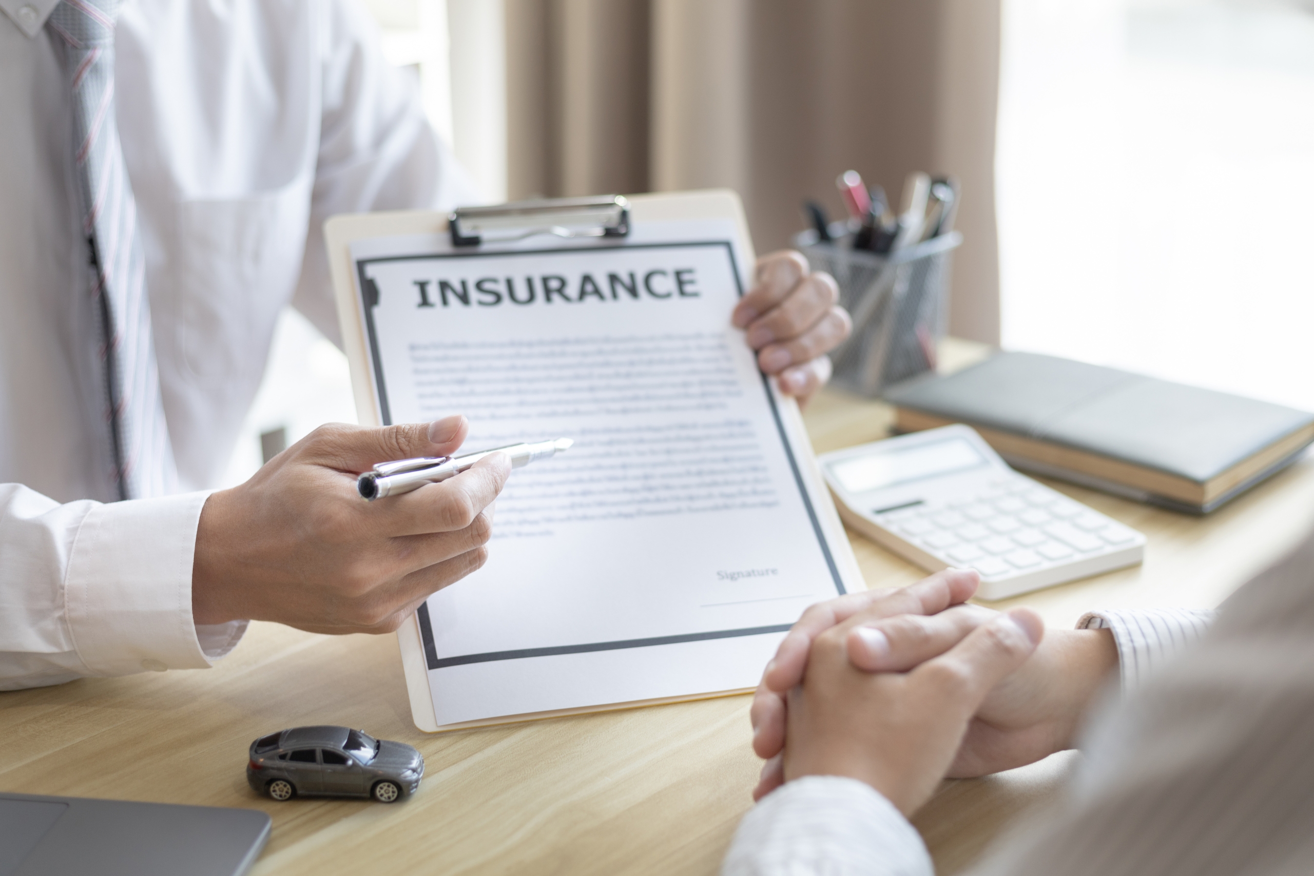 Person explaining car insurance document to a client at desk.