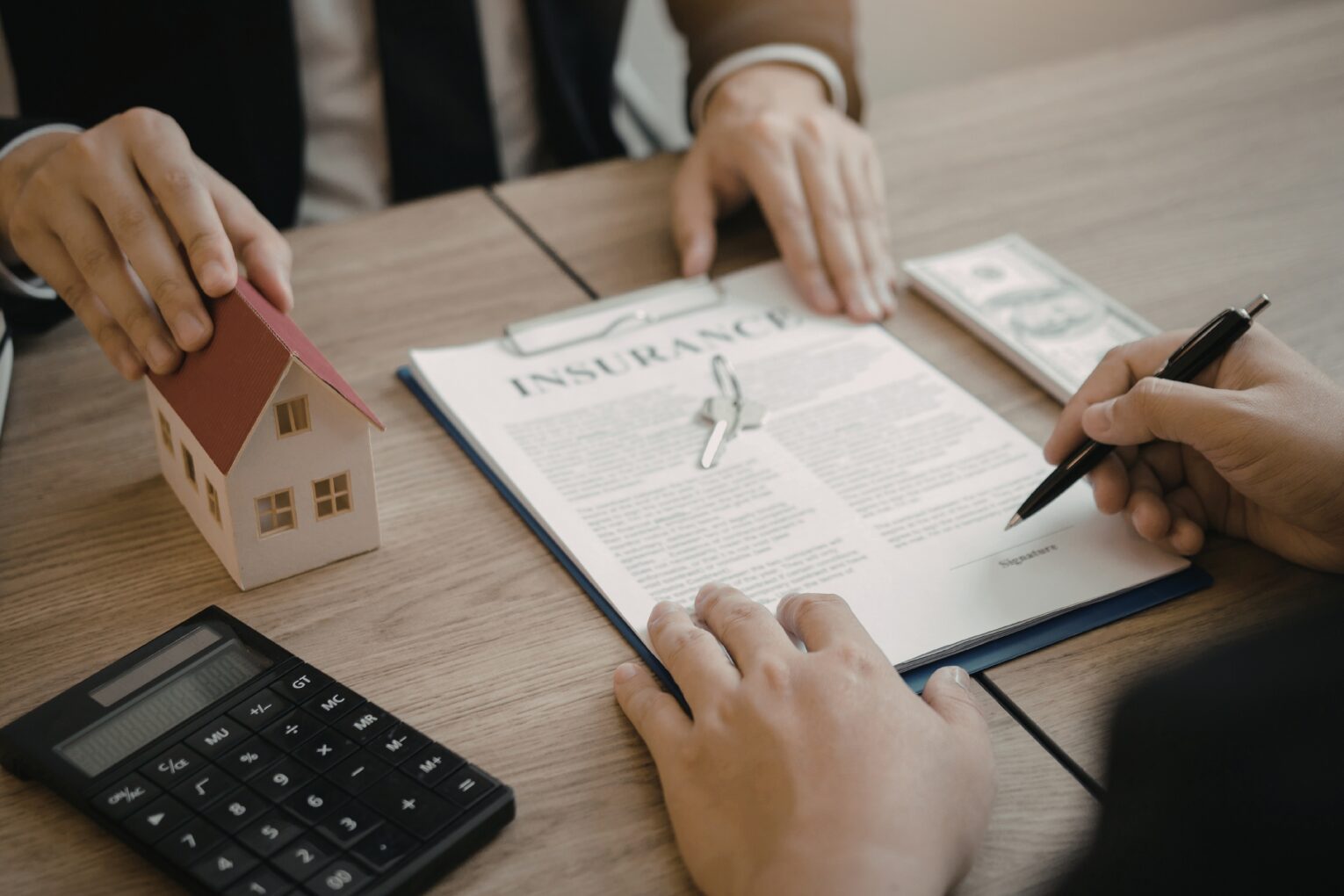 People discussing and signing a home insurance contract with keys and money on the table.