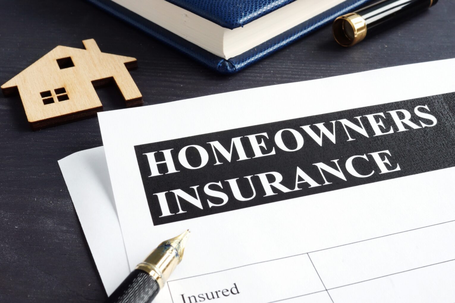 Homeowners insurance document with pen and house model on desk.